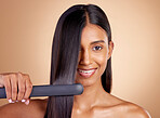 Portrait, hair and flat iron with a woman in studio on a beige background for beauty or style. Face, smile and haircare with happy young female model using a straightener appliance for natural care