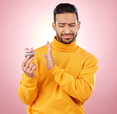 Buy stock photo Man, cupcake and studio for diet choice, thinking or bad review for gluten allergy, health or pink background. Gen z guy, student or fashion model with muffin, cake or decision for nutrition feedback