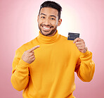 Man, pointing and credit card with finance, payment and loan, budget and fashion sale on studio pink background. Portrait, banking and happy asian person or gen z with retail transaction or shopping