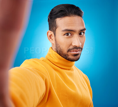Buy stock photo Selfie, face and portrait of a young man in studio with hand, style and fashion clothes. Serious male asian model on a blue background for social media, platform or network profile picture update