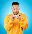 Phone, reading and a shocked man in studio with a secret, gossip or fake news on social media. Male asian model watch video or post on smartphone for wow, surprise or chat on a blue background