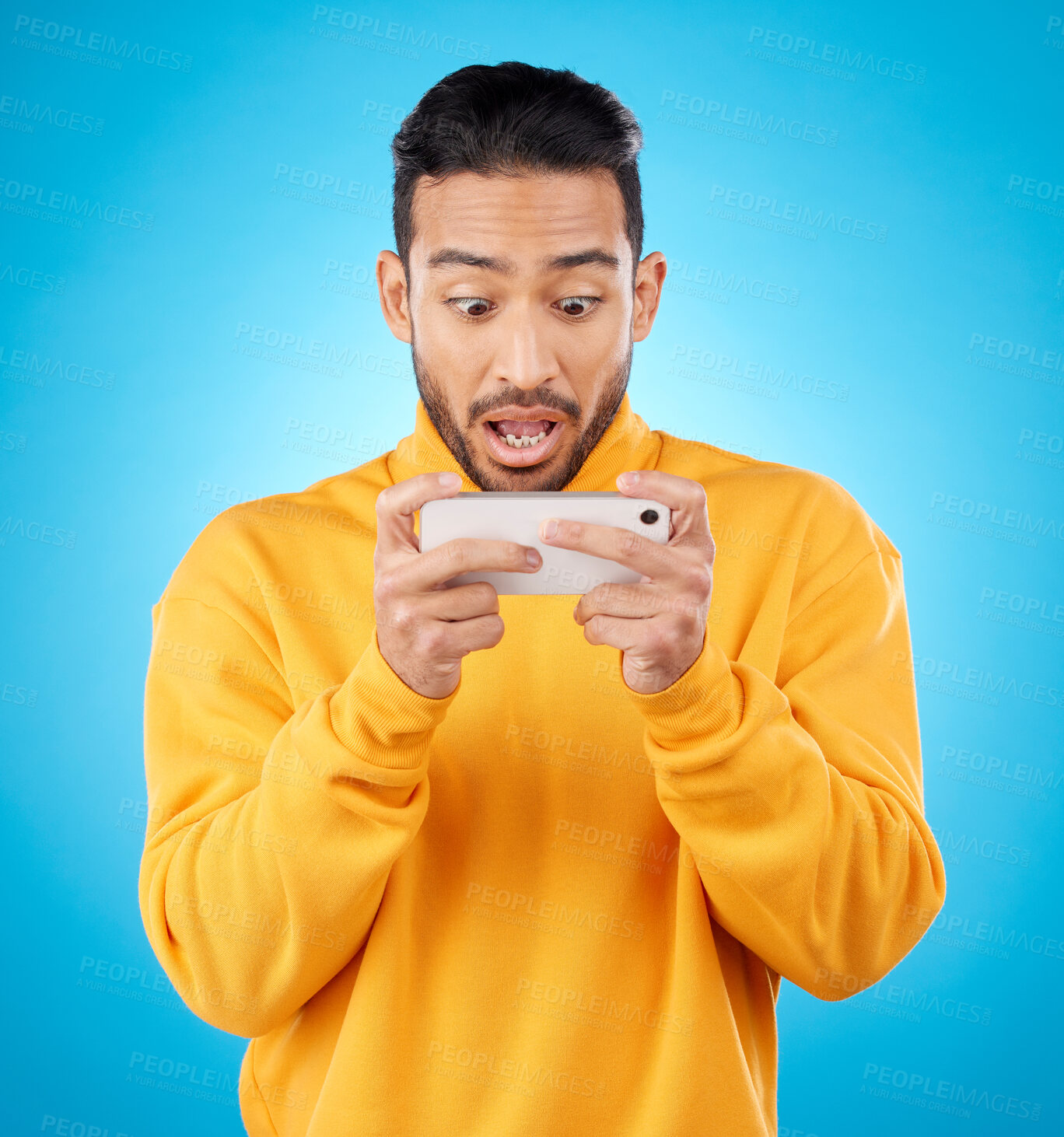 Buy stock photo Phone, reading and a shocked man in studio with a secret, gossip or fake news on social media. Male asian model watch video or post on smartphone for wow, surprise or chat on a blue background