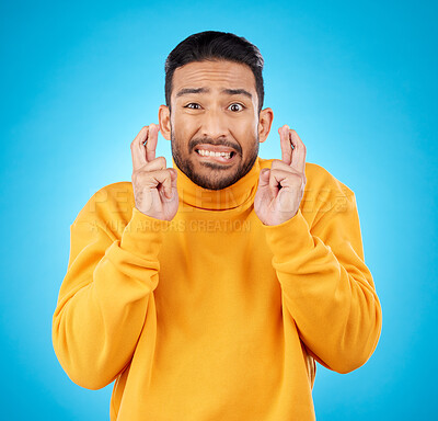 Buy stock photo Nervous, portrait and fingers crossed by asian man with anxiety in studio for news, feedback or review on blue background. Hand, emoji and face of guy with stress for results, competition or giveaway