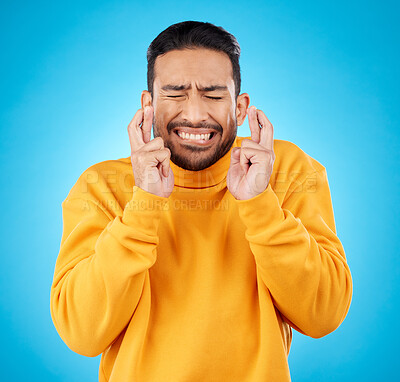 Buy stock photo Nervous, eyes closed and fingers crossed by asian man with anxiety in studio for news, feedback or review on blue background. Hand, emoji and guy with stress for results, competition or giveaway