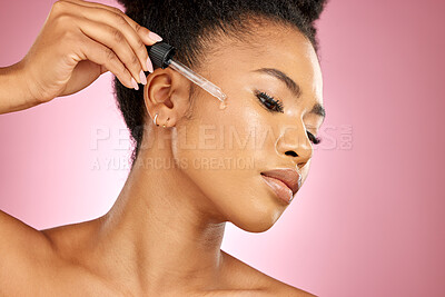 Buy stock photo Black woman, oil and serum on face, skincare shine or aesthetic dermatology on pink background in studio. Female model, facial cosmetics and dropper of hyaluronic acid, liquid collagen or beauty glow