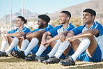Happy soccer players, relax or team on a field for a sports game together in summer on resting break. Smile, stadium or group of football athletes sitting after fitness exercise, training or match