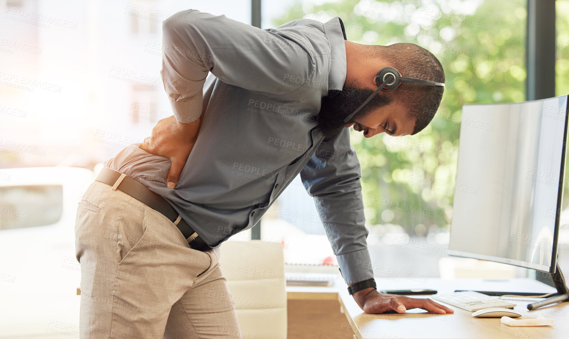 Buy stock photo Call center, back pain and a black man consultant in his office, standing while holding is spine. Injury, customer service or support and a young male employee with muscle strain in a crm workplace