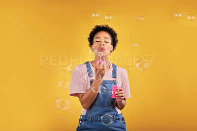 Buy stock photo Woman, blowing bubbles and fun in studio while playful for birthday, happiness or party celebration. Black female model person with liquid soap, natural beauty and fashion on a yellow background