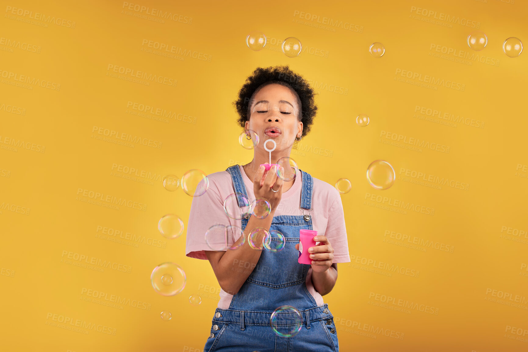 Buy stock photo Woman, blowing bubbles and fun in studio while playful for birthday, happiness or party celebration. Black female model person with liquid soap, natural beauty and fashion on a yellow background