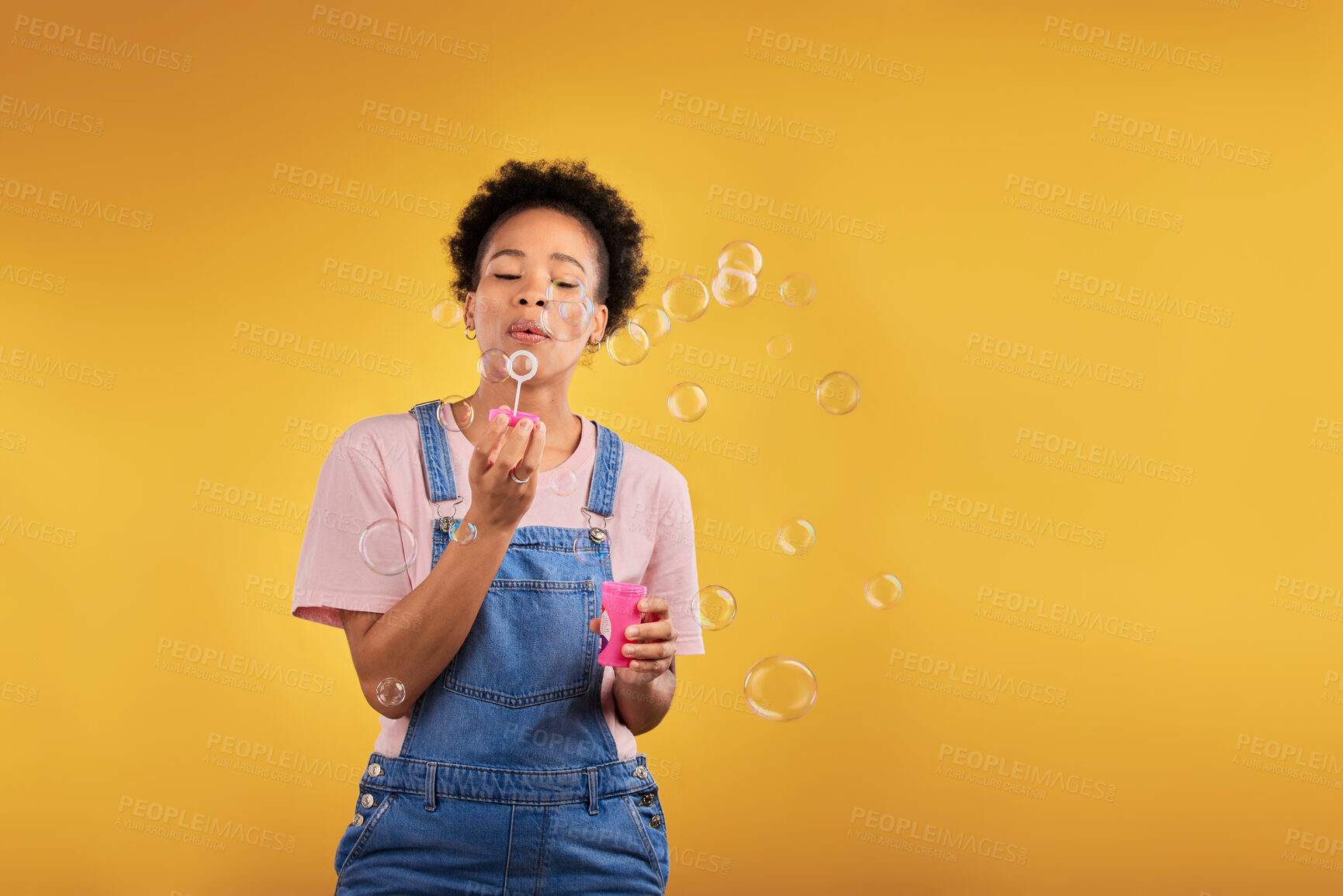 Buy stock photo Blowing bubbles, woman and fun in studio while playful for birthday or party celebration. Black female model person with liquid soap, natural beauty and fashion on a yellow background with space