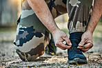 Man, hands and tying shoes in army getting ready for war, battle or fight on ground in nature. Closeup of male person tie shoe lace in preparation for training, exercise or gear in self defense