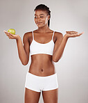 Choice, apple and black woman with chocolate for health decision and isolated in gray studio background with junk food. Balance, wellness and African person holding fruit and sweet, dessert or candy