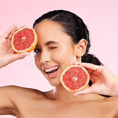 Buy stock photo Face, beauty and woman wink with grapefruit in studio isolated on a pink background. Portrait, natural cosmetic and model with fruit, food or nutrition for skincare, healthy vegan diet or vitamin c