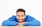 Thinking, wonder and face of man on a white background with ideas, brainstorming and thoughtful by table. Happy, smile and face of isolated male person rest on desk for choice or decision in studio