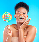 Candy, portrait and woman with sprinkles on her lips in a studio with sweet treats, dessert or snack. Happy, smile and young African female model with a colorful lollipop isolated by blue background.