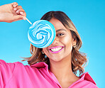Woman, lollipop eye and studio portrait for eating, sweets and comic smile with food by blue background. Girl, student or young fashion model with candy, beauty and funny with sugar for dessert snack