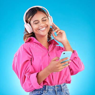 Buy stock photo Phone, music and headphones with a woman in studio on a blue background, listening to the radio. Mobile, smile and a happy young female person streaming audio to relax for wellness or freedom