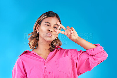 Buy stock photo Wink, kiss and peace sign with portrait of woman in studio for support, gen z and emoji. Motivation, kindness and winner with face of person on blue background for v icon, positive and symbol