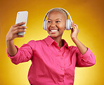 Smile, selfie and black woman with headphones for music, radio and podcast in studio isolated on a yellow background. Profile picture, photographer and African person or influencer on social media