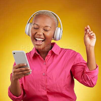 Buy stock photo Phone, headphones for music and black woman singing along to radio, sound or podcast in studio isolated on a yellow background. Happy, audio and African person listen, streaming and dance with energy