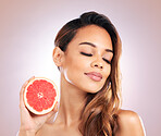 Calm woman, grapefruit and vitamin C for skincare or beauty against a studio background. Face of female person or model in relax with organic fruit for natural nutrition, diet or healthy wellness