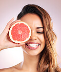 Citrus, grapefruit and face of woman with healthy, natural or organic beauty isolated in a brown studio background. Excited, eyes and young female person with vitamin c for skincare or detox