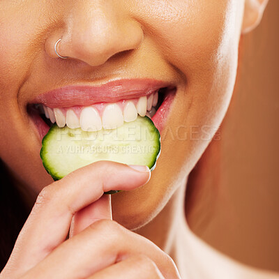 Buy stock photo Woman, mouth or eating a cucumber for skincare nutrition or healthy diet against a brown studio background. Smile, bite or closeup of girl vegetable for organic facial treatment or natural cosmetics