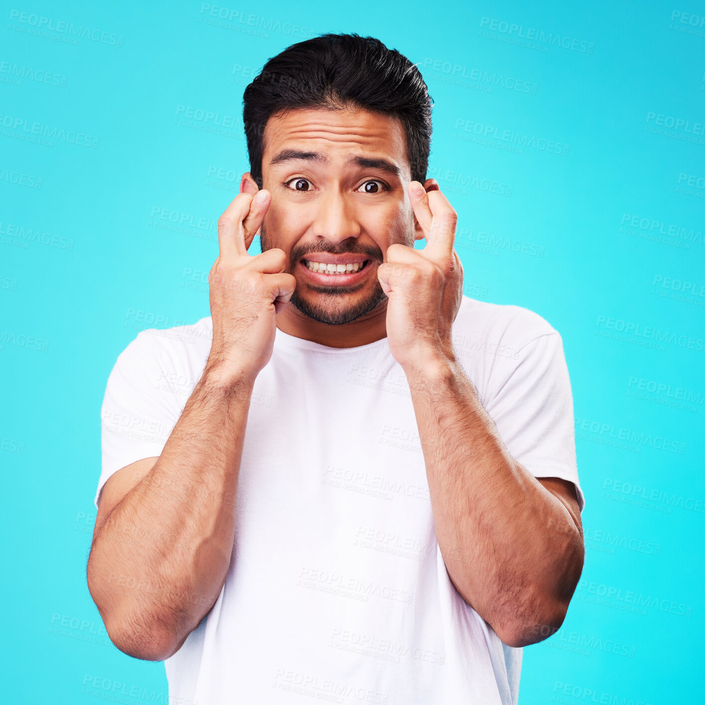 Buy stock photo Fear, hope and portrait of man fingers crossed, anxiety or nervous due to crisis or stress isolated in studio blue background. Worry, suspense and young male person hands in face for mistake reaction