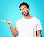 Gesture, hand and portrait of a man on a blue background for marketing, advertising or a logo. Smile, promo and an Asian person showing mockup space for branding isolated on a studio backdrop