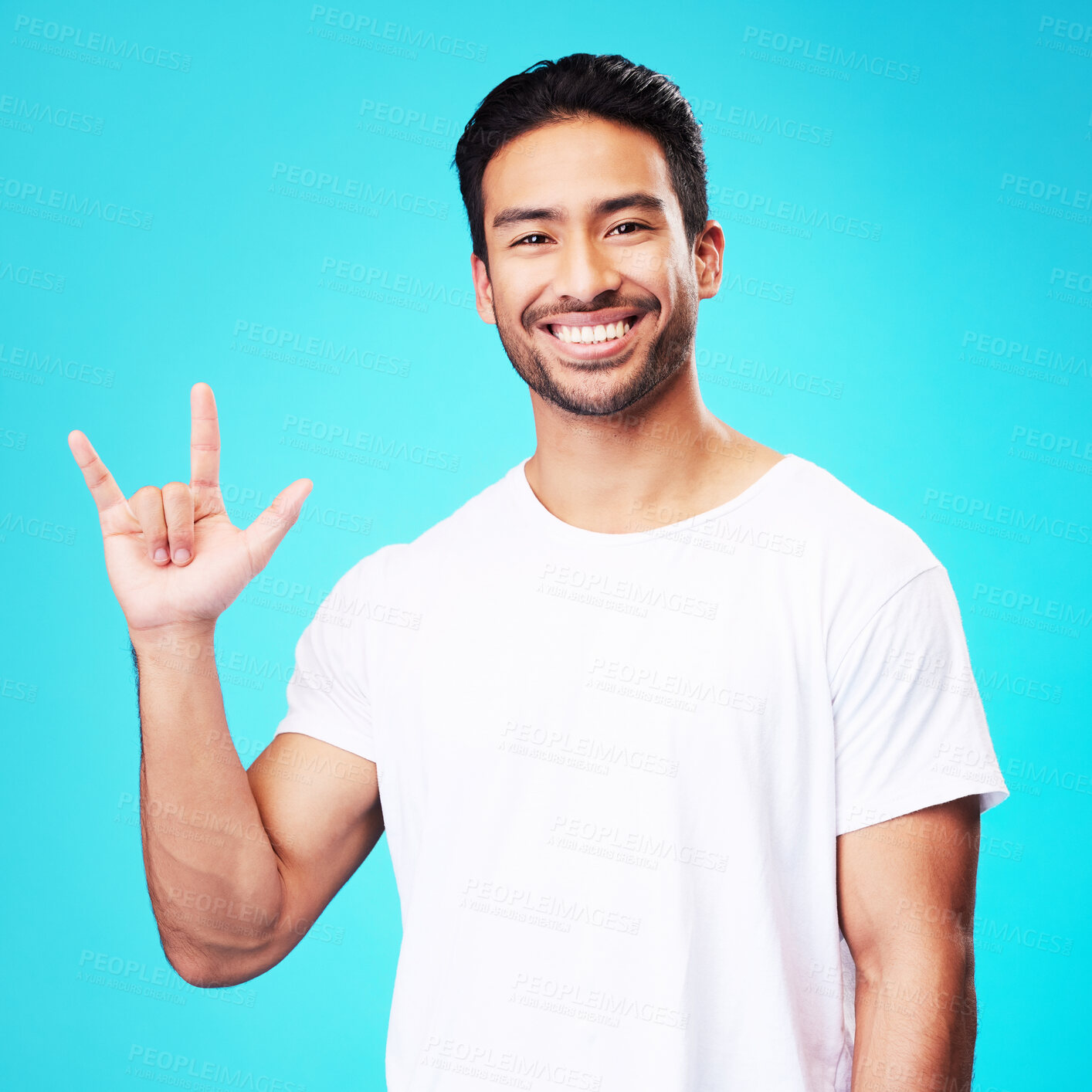 Buy stock photo Man, horns and love in studio portrait with smile, kindness and sign language by blue background. Young guy, student and happy with icon, emoji and hand with care, romance or vote with white t-shirt