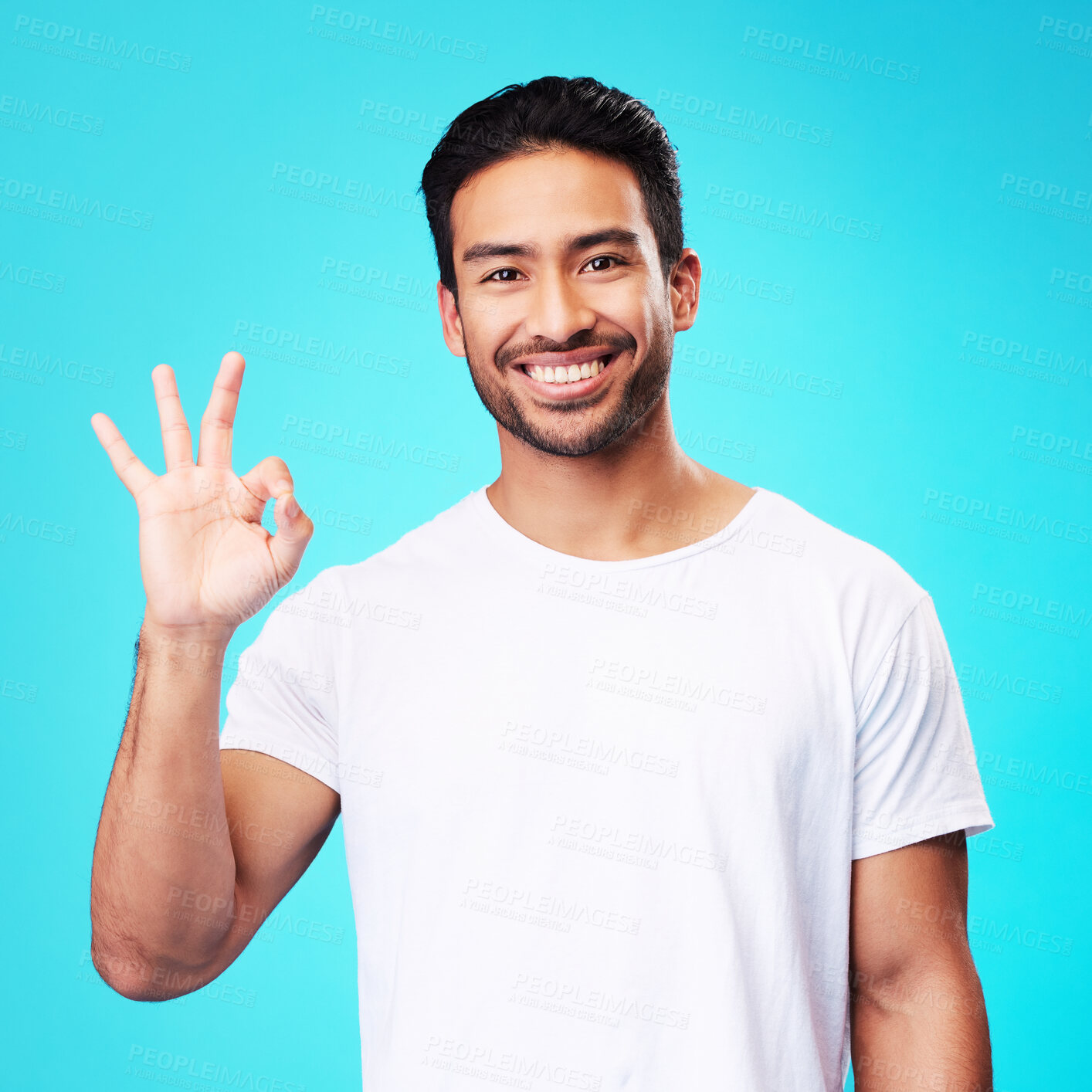 Buy stock photo Happy, perfect gesture and portrait of a man in a studio with an agreement sign or expression. Happiness, smile and young Indian male model with an approval hand emoji isolated by a blue background.