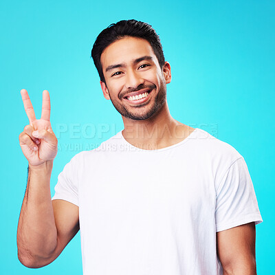 Buy stock photo Portrait, man and peace fingers in studio for hope, self love and show icon on blue background. Face of happy asian male model, v sign and hands for victory, good mood and emoji in support of freedom