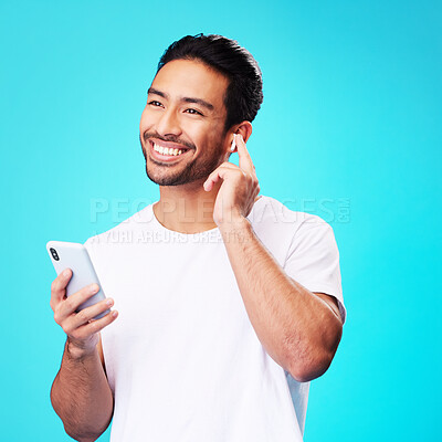 Buy stock photo Asian man, earphones and smartphone in studio for music, podcast app and blue background. Happy male model thinking with mobile phone, listening to audio and streaming sound of radio media with tech