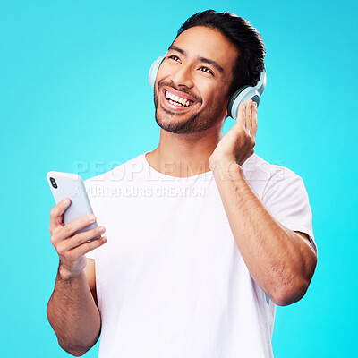 Buy stock photo Music, headphones and Asian man with phone for listening in studio isolated on a blue background. Radio, smile and person with audio, sound and hearing podcast, jazz or media for hip hop with mobile