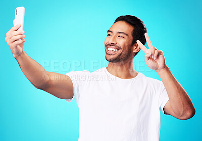 Buy stock photo Happy, peace sign and a man with a phone on a blue background for communication or social media. Smile, contact and a male influencer with an emoji hand and a mobile while live streaming in studio
