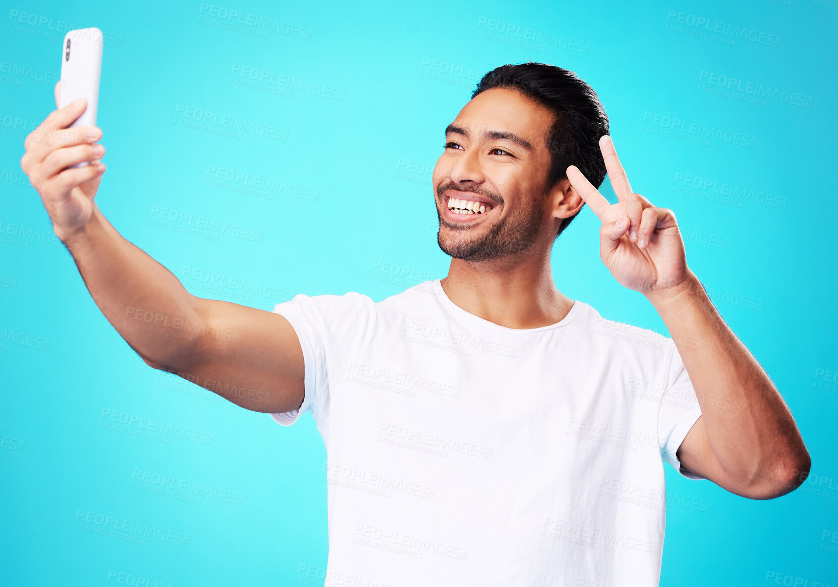 Buy stock photo Happy, peace sign and a man with a phone on a blue background for communication or social media. Smile, contact and a male influencer with an emoji hand and a mobile while live streaming in studio