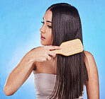 Hair care, beauty and a woman with a brush in studio for self love, hygiene and shine. Salon, hairdresser and a female model person with shampoo, cosmetics and a hairbrush on a blue background