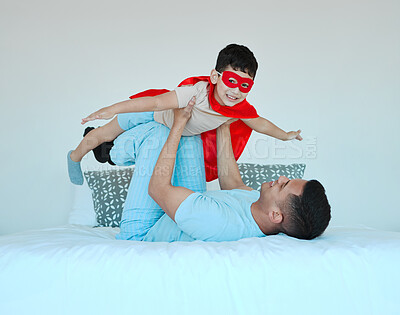 Buy stock photo Bonding, bedroom and father playing with his child for quality time, fun or happiness at home. Happy, smile and young dad relaxing with his boy kid in a superhero costume on the bed at family house.