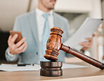 Closeup, gavel and law firm on table, office or attorney man in blurred background, phone texting or networking. Advocate, lawyer or judge with legal hammer, reading and documents for court evidence