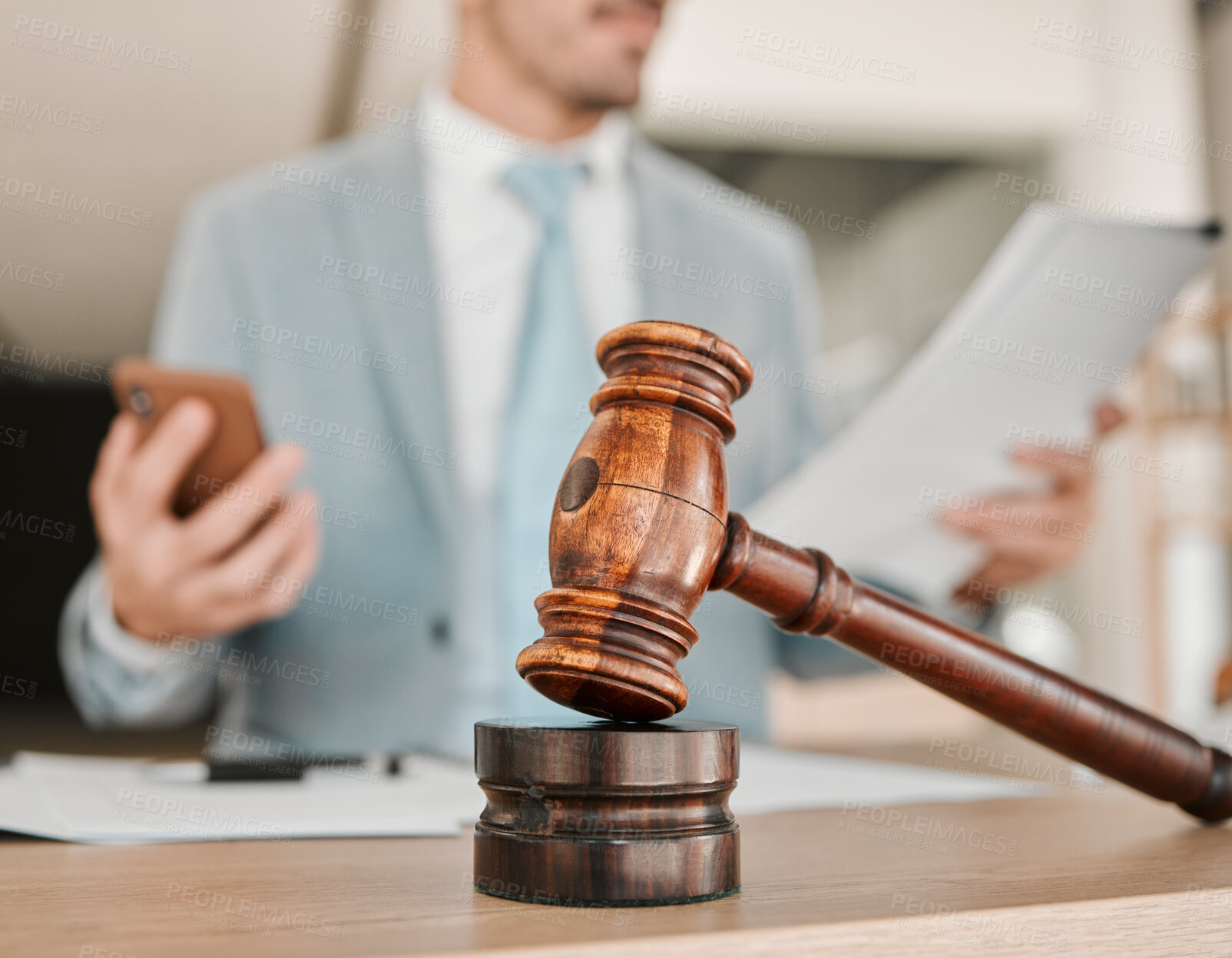 Buy stock photo Closeup, gavel and law firm on table, office or attorney man in blurred background, phone texting or networking. Advocate, lawyer or judge with legal hammer, reading and documents for court evidence