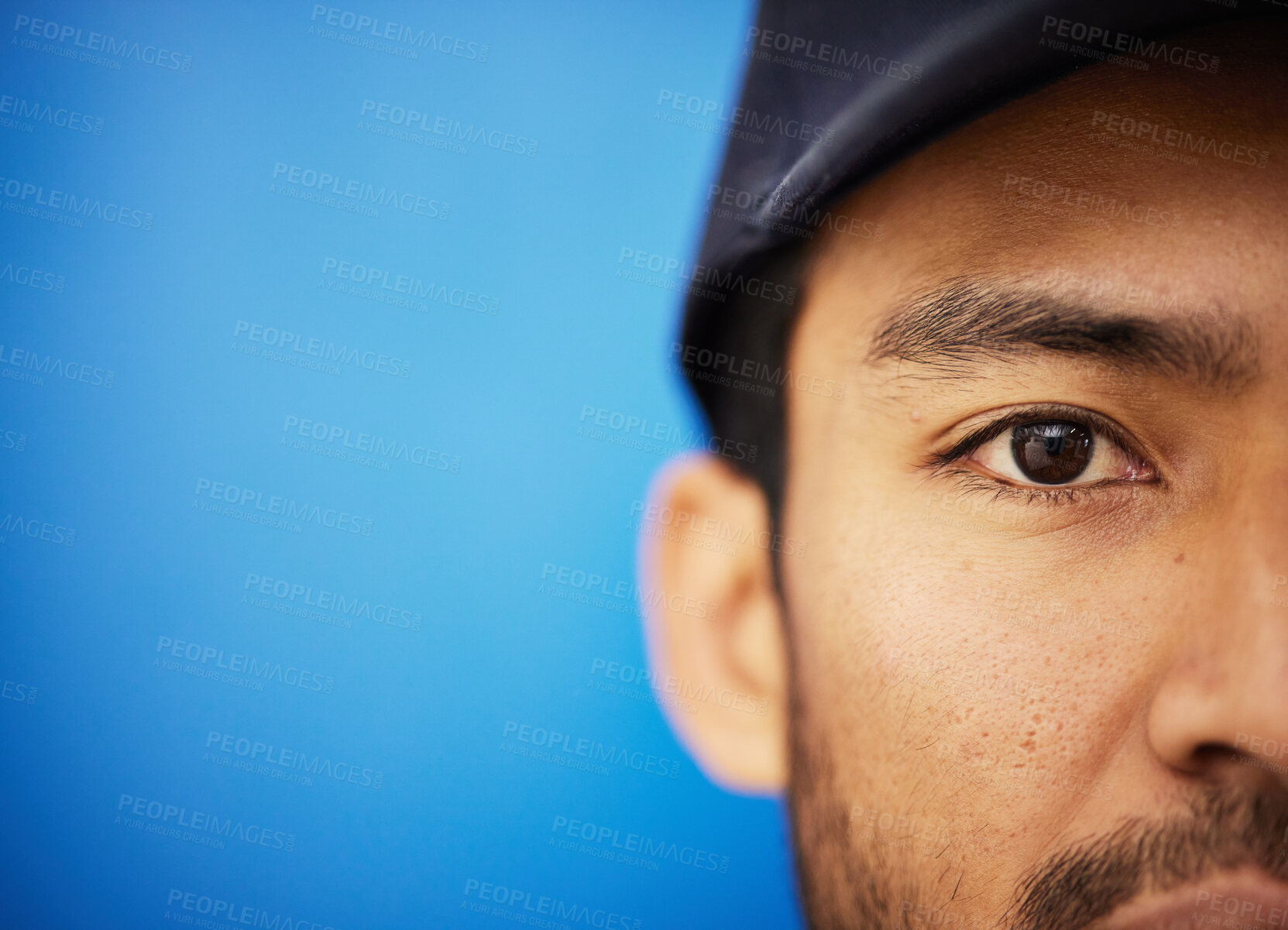 Buy stock photo Eye, closeup and portrait of half of man in sports on blue background with advertising, mockup or space with athlete in studio. Serious, face and Indian person in cricket or baseball cap and fitness