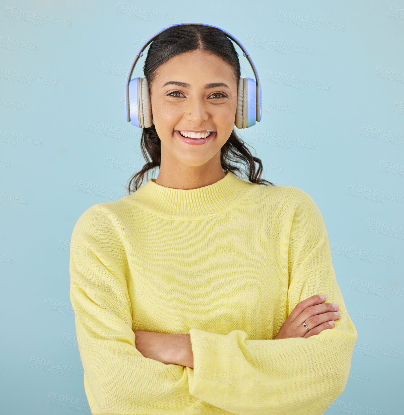 Buy stock photo Portrait of woman, headphones and smile in studio listening to podcast, mobile app and streaming radio site. Sound, music media subscription and happy girl with arms crossed on blue background space.
