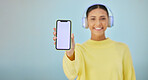 Happy woman with phone screen, headphones and mockup in studio for social media post, mobile app and streaming radio. Smile, music media subscription and girl with cellphone on blue background space.