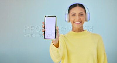 Buy stock photo Happy woman with phone screen, headphones and mockup in studio for social media post, mobile app and streaming radio. Smile, music media subscription and girl with cellphone on blue background space.