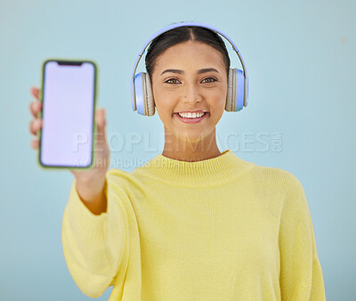Buy stock photo Portrait of happy woman with phone screen, headphones and mockup in studio for social media, mobile app and streaming radio. Smile, music subscription and girl with cellphone on blue background space