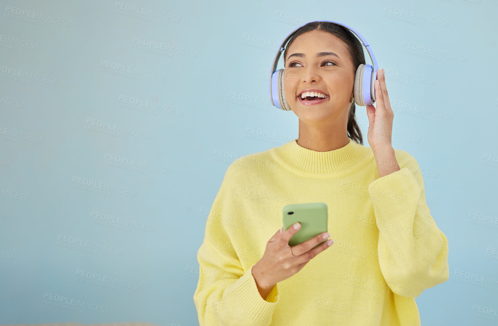 Buy stock photo Happy woman with phone, headphones and banner mockup in studio on social media, mobile app and streaming radio. Smile, relax and music media subscription, girl with cellphone on blue background space