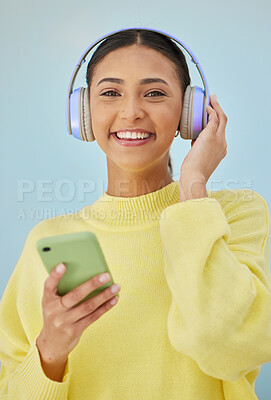 Buy stock photo Portrait of woman with phone, headphones and smile in studio for social media, mobile app and streaming radio site. Podcast, music media subscription and happy girl with cellphone on blue background.