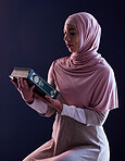 Quran, faith and muslim woman reading in a studio with traditional clothes and hijab. Serious, religion and young islamic female person studying the holy Arabic book isolated by a black background.