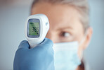 Woman in face mask, hand of doctor and thermometer in hospital for covid test, safety and healthcare consultation. Temperature check, corona and patient at clinic with medical professional for exam.