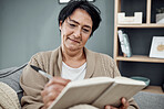 Smile, relax and an old woman writing in her diary while sitting in the living room of her retirement home. Notebook, pen and a happy senior female pensioner on a sofa, taking notes in a journal